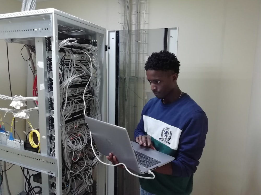  a person holding a laptop while standing next to computer equipment