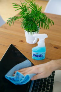 a person cleaning a laptop screen with a blue microfiber cloth and cleaning solution