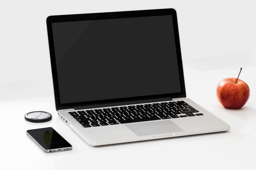A phone and an apple placed next to a laptop.