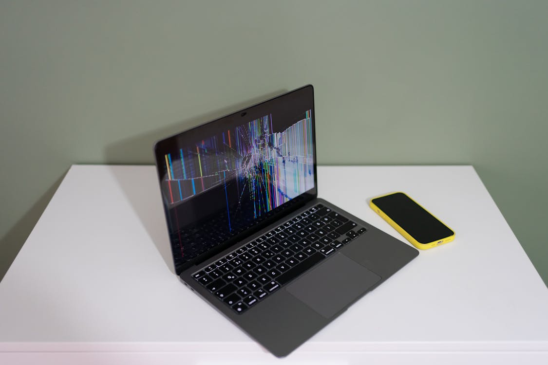A sleek laptop placed on a white table with a broken screen.